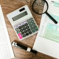 Une calculatrice, une loupe, un marqueur noir, un formulaire fiscal et des documents financiers pour un externalisation comptable.